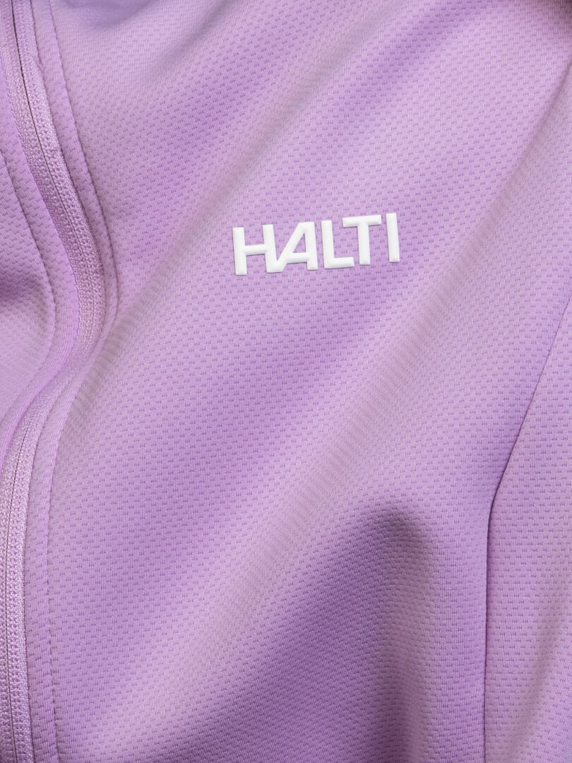 Lähikuva laventelinsävyisestä Halti Kivikko Välitakki Naisten -takista, jossa on näkyvä vetoketju ja valkoinen Halti-logo kankaassa.