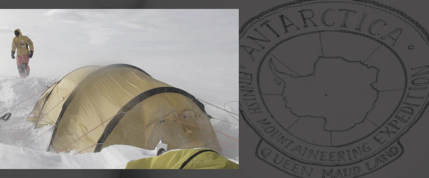 Kylmävarusteisiin pukeutunut henkilö seisoo keltaisen teltan vieressä lumisessa ja tuulisessa Etelämantereella.