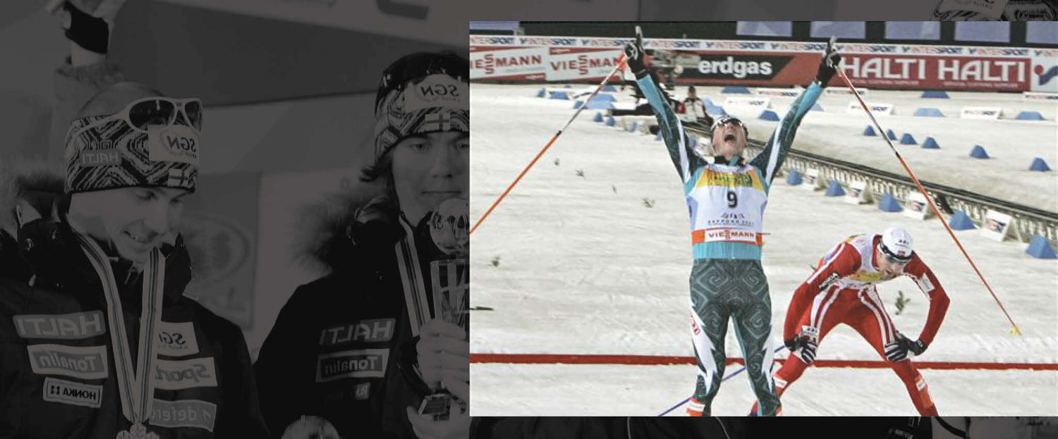 Vihreäpukuinen hiihtäjä nostaa kätensä voittajana maalissa, kun toinen punapukuinen hiihtäjä tulee maaliin aivan perässä.