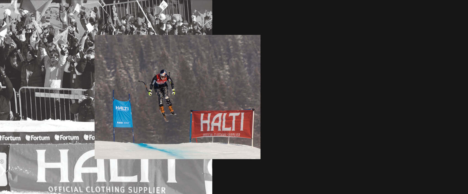 Ilmassa hiihtäjä kilpailee ja kulkee kahden Halti-tuotemerkillä varustetun banderollin ja lumessa olevan sinisen viivan välissä.