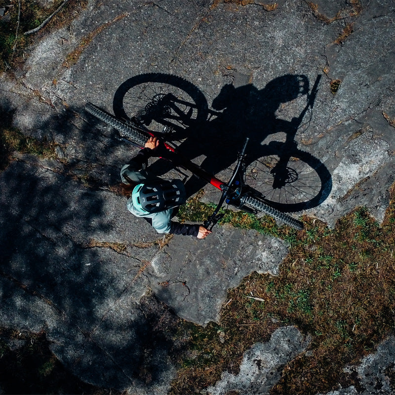 Kypäräpäinen henkilö seisoo polkupyörän kanssa kivikkoisella pinnalla ja heittää selkeän varjon.