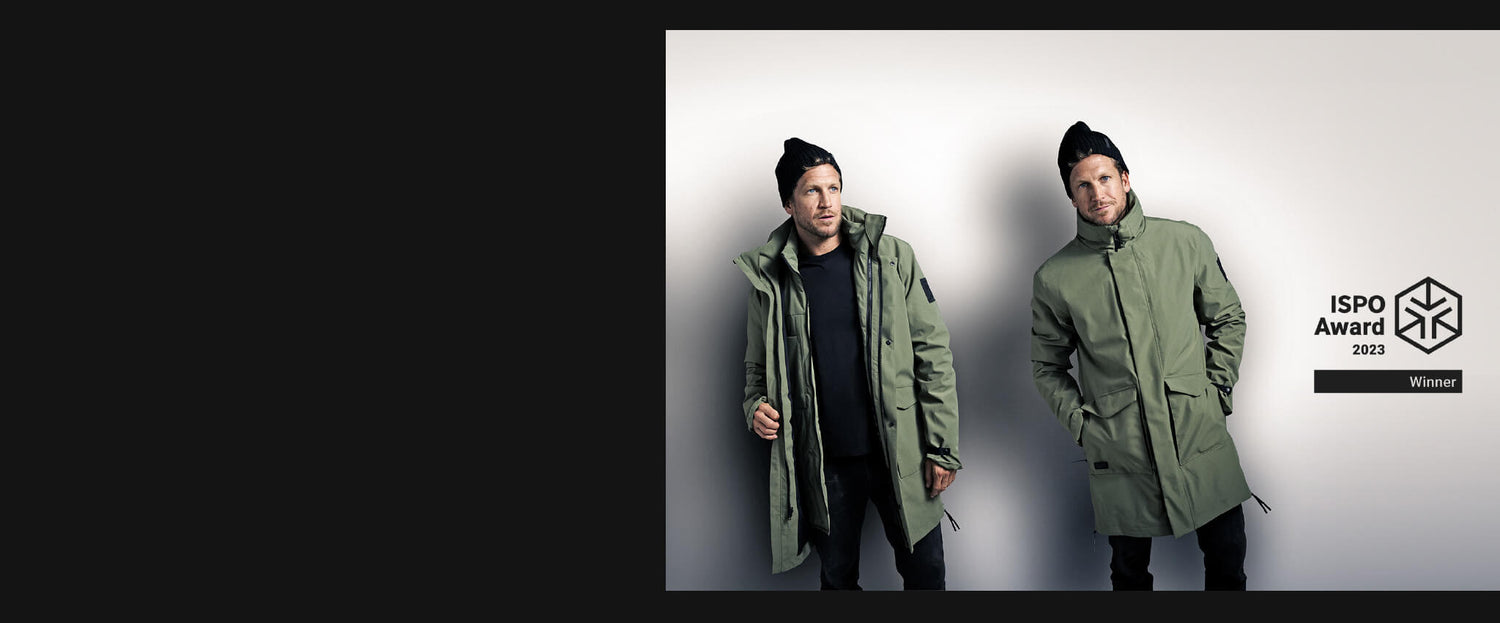 Kaksi vihreisiin takkeihin ja mustiin pipoihin pukeutunutta miestä seisoo ISPO Award 2023 Winner -logon vieressä valkoisella pohjalla.