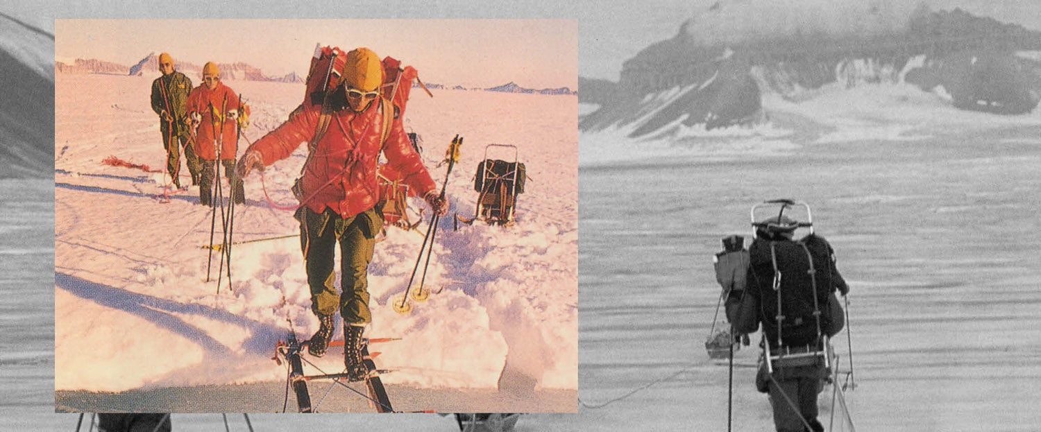 Useat talvivarusteisiin ja suksiin pukeutuneet ihmiset kulkevat lumisessa maisemassa vetäen perässään tarvikkeita sisältäviä rekiä.