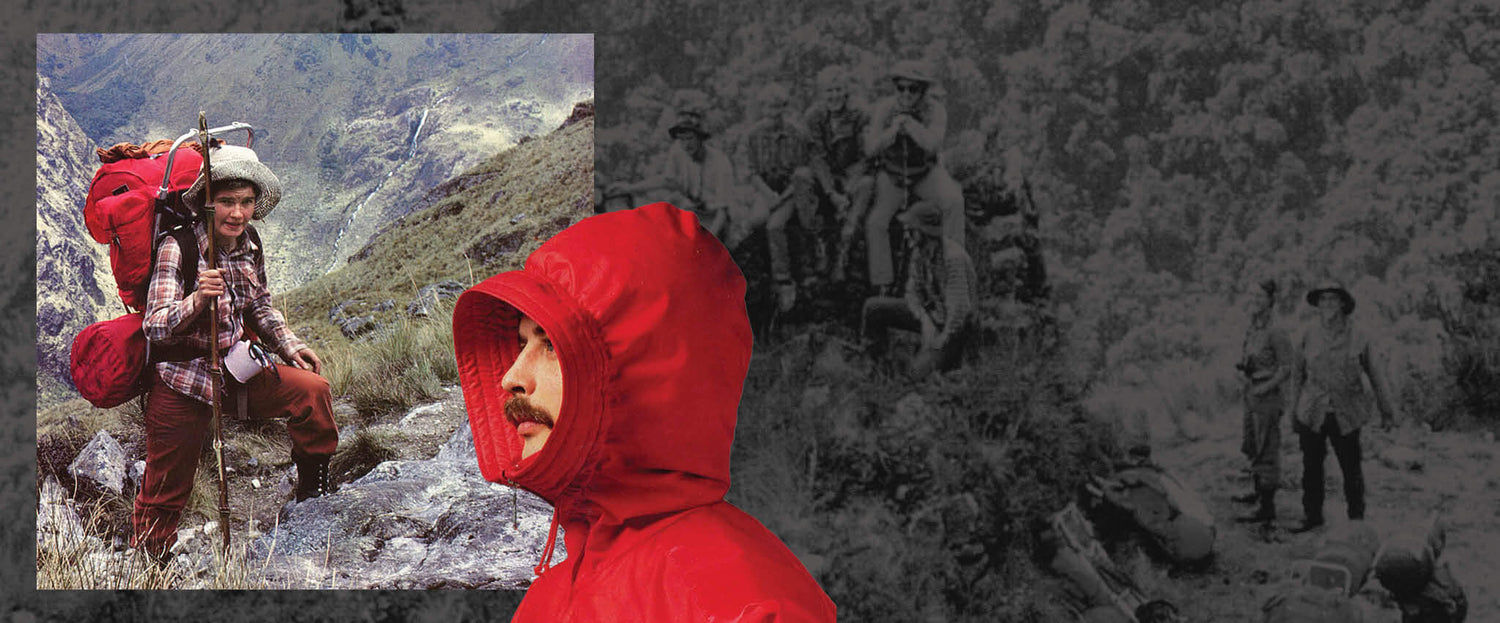 Punaiseen sadetakkiin pukeutunut mies seisoo vanhan valokuvan edessä, jossa on vuoristossa vaeltajia, joista yksi kantaa punaista reppua.