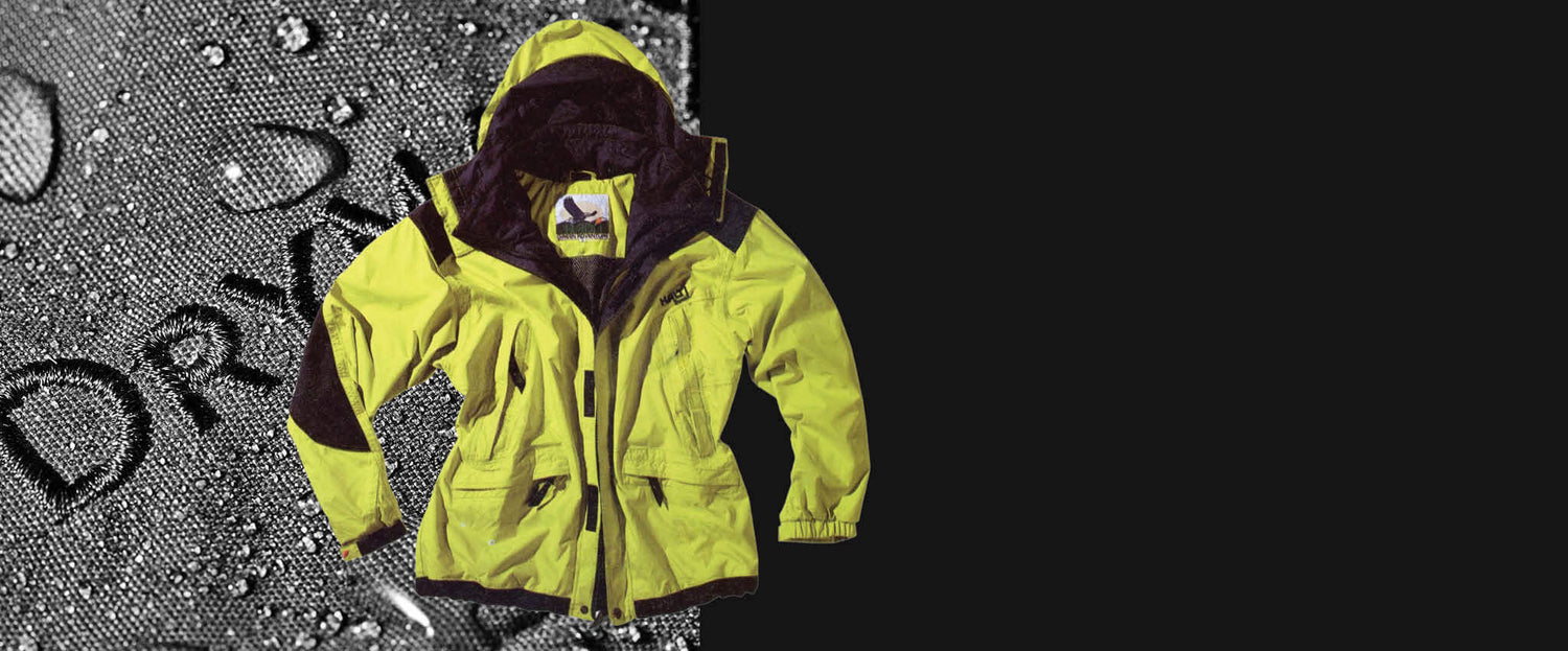 Keltainen vedenpitävä takki on esillä; taustalla on vesipisaroita, jotka peittävät harmaata pintaa.