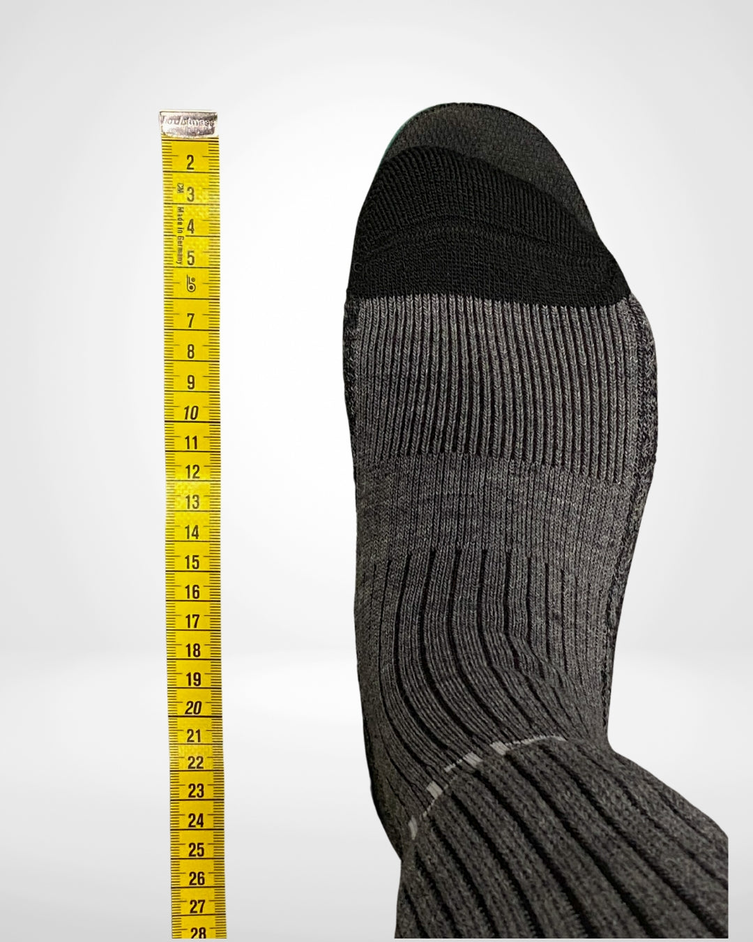 Jalka harmaassa sukassa on keltaisen mittanauhan vieressä, jonka pituus on noin 27 senttimetriä.