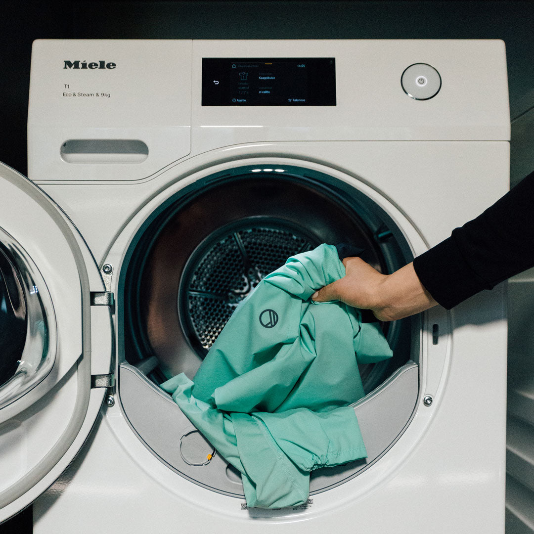 Henkilö lataa vaaleanvihreän vaatteen Miele-pesukoneeseen.