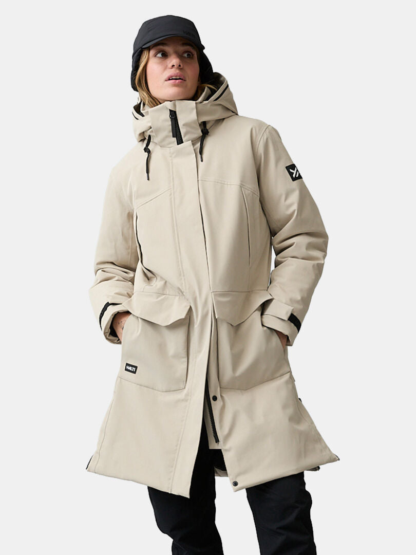 Halti Kallio DX -naisten parka, beige, hupulla, mustilla yksityiskohdilla ja taskuilla, yhdistettynä mustaan lippalakkiin.