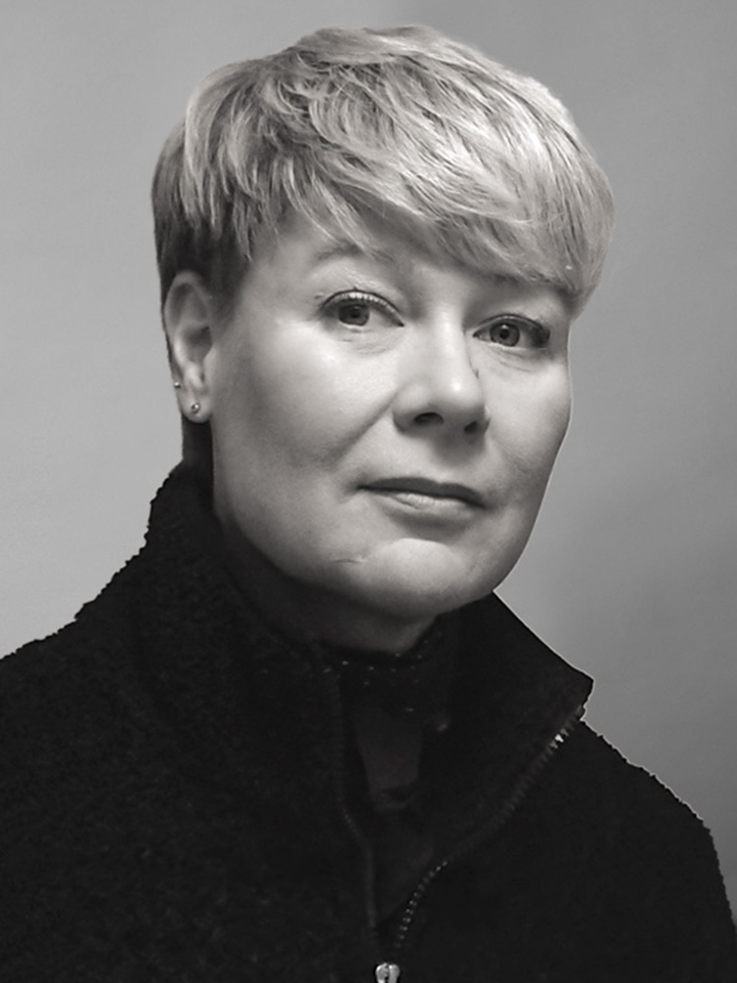 Henkilö, jolla on lyhyet, vaaleat hiukset ja tumma takki, katsoo kameraan neutraalilla ilmeellä.