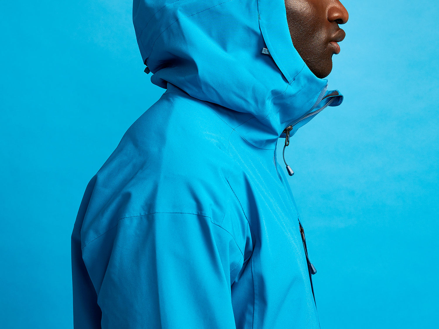 Henkilö, jolla on kirkkaansininen hupullinen takki ja samanlainen sininen tausta, sivulta kuvattuna.