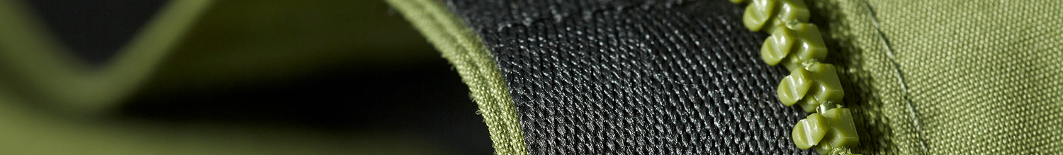 Lähikuva vihreästä vetoketjusta kankaan pinnalla, jossa näkyvät yksityiskohtaisesti hampaat ja ympäröivä materiaali.