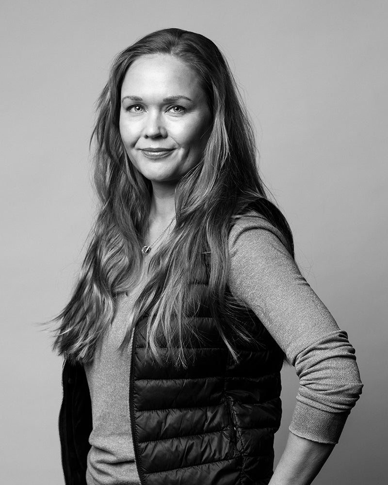 Pitkätukkainen nainen, jolla on vaalea villapaita ja puskuriliivi, seisoo toinen käsi lantiollaan kameraan päin.