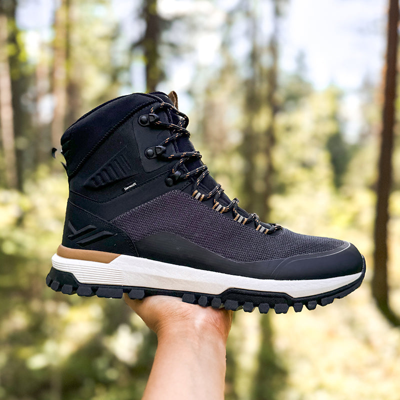 Henkilö pitelee kädessään karheapohjaista Halti Kajava DrymaxX Ulkoilukenkä Naisten kenkää sumeaa metsätaustaa vasten.