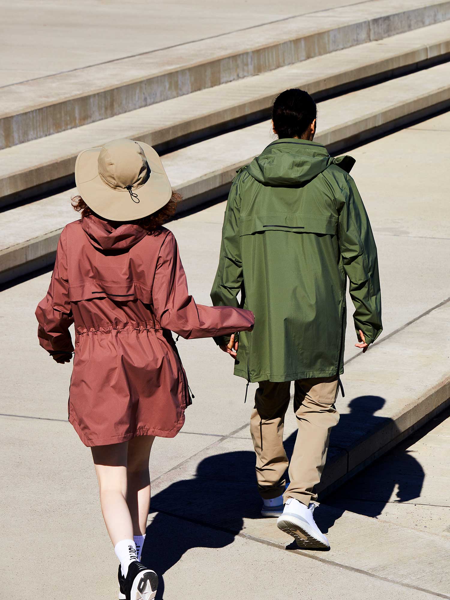 Kaksi takkiin pukeutunutta henkilöä kävelee ulkona betonipinnalla, jossa on portaita, kuvattu takaapäin.