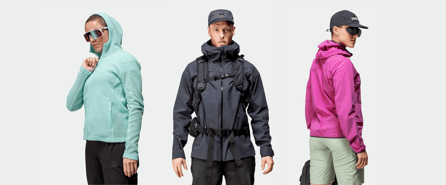 Kolme henkilöä, joilla on ulkoiluvarusteet: tiilenpunainen huppari, tumma takki, jossa on hihnat, ja magentanpunainen takki, jossa on lippis ja shortsit.