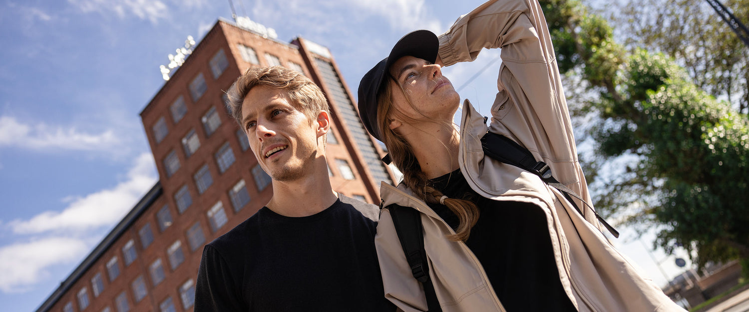 Mies ja nainen seisovat ulkona tiilirakennuksen vieressä aurinkoisena päivänä ja katselevat kaukaisuuteen.