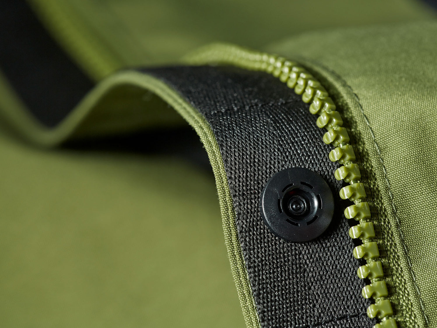 Lähikuva vihreästä vetoketjusta ja mustasta napista vihreällä kankaalla.