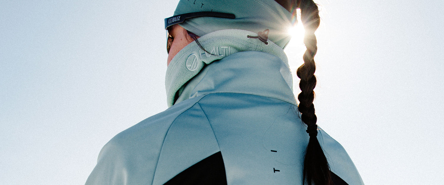 Henkilö, jolla on vaaleansininen takki ja pipo, pitkät letit, seisoo ulkona kirkkaassa auringonvalossa.