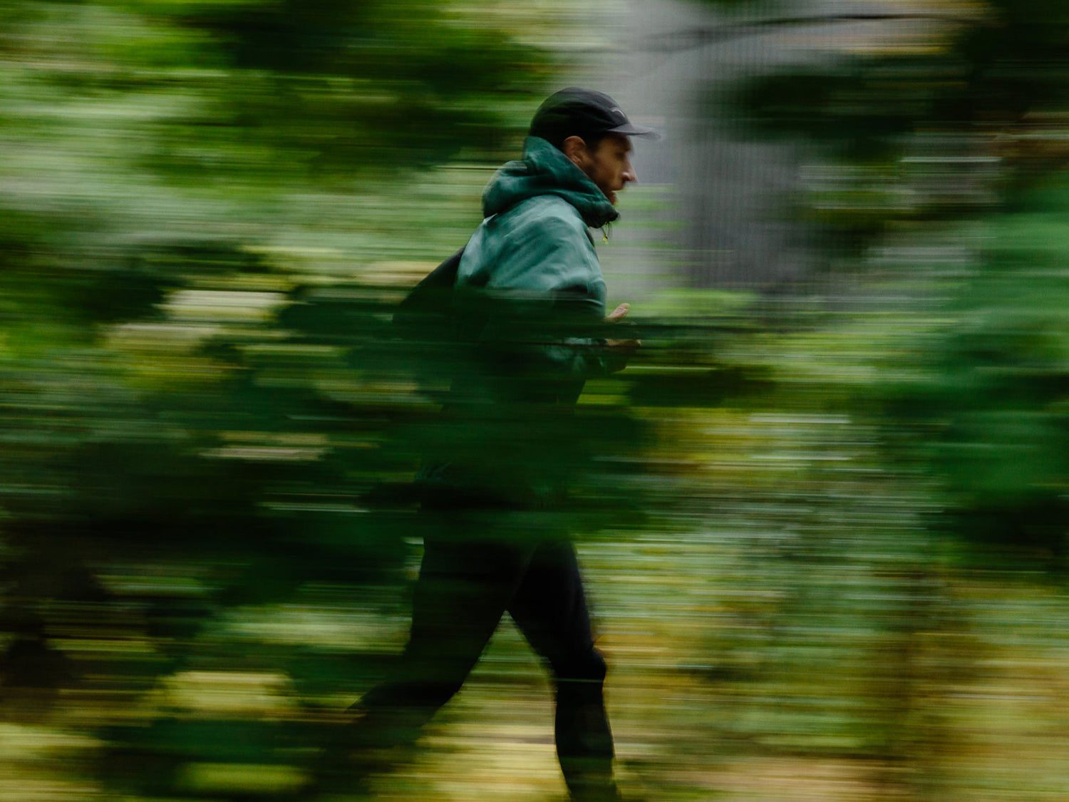 Tumma lippalakki ja takki päällään oleva henkilö juoksee hämärtyneessä, vihreässä ulkoilmakuvassa, mikä viittaa liikkeeseen.