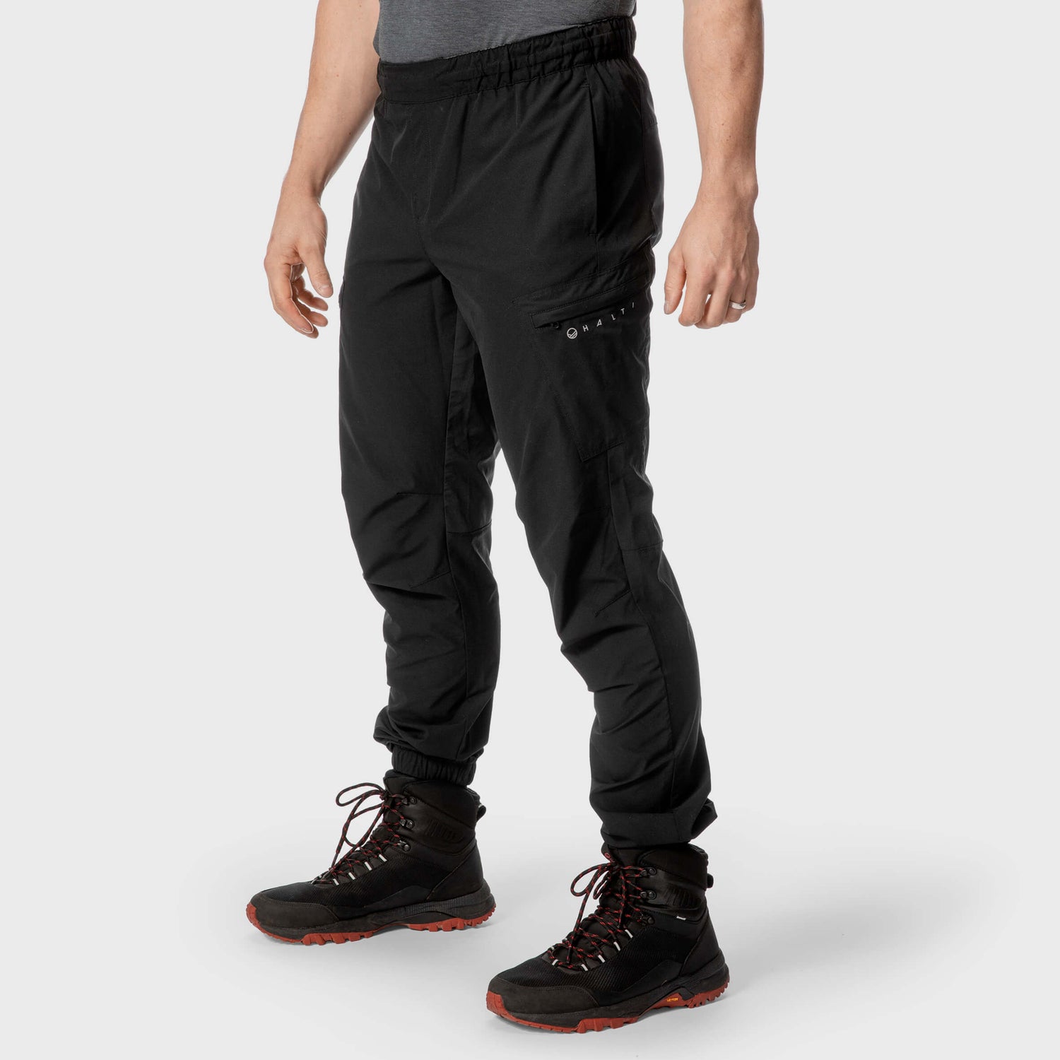 Henkilöllä on mustat lenkkihousut ja mustat vaelluskengät, joissa on oranssit pohjat, ja hän seisoo vaaleaa taustaa vasten.