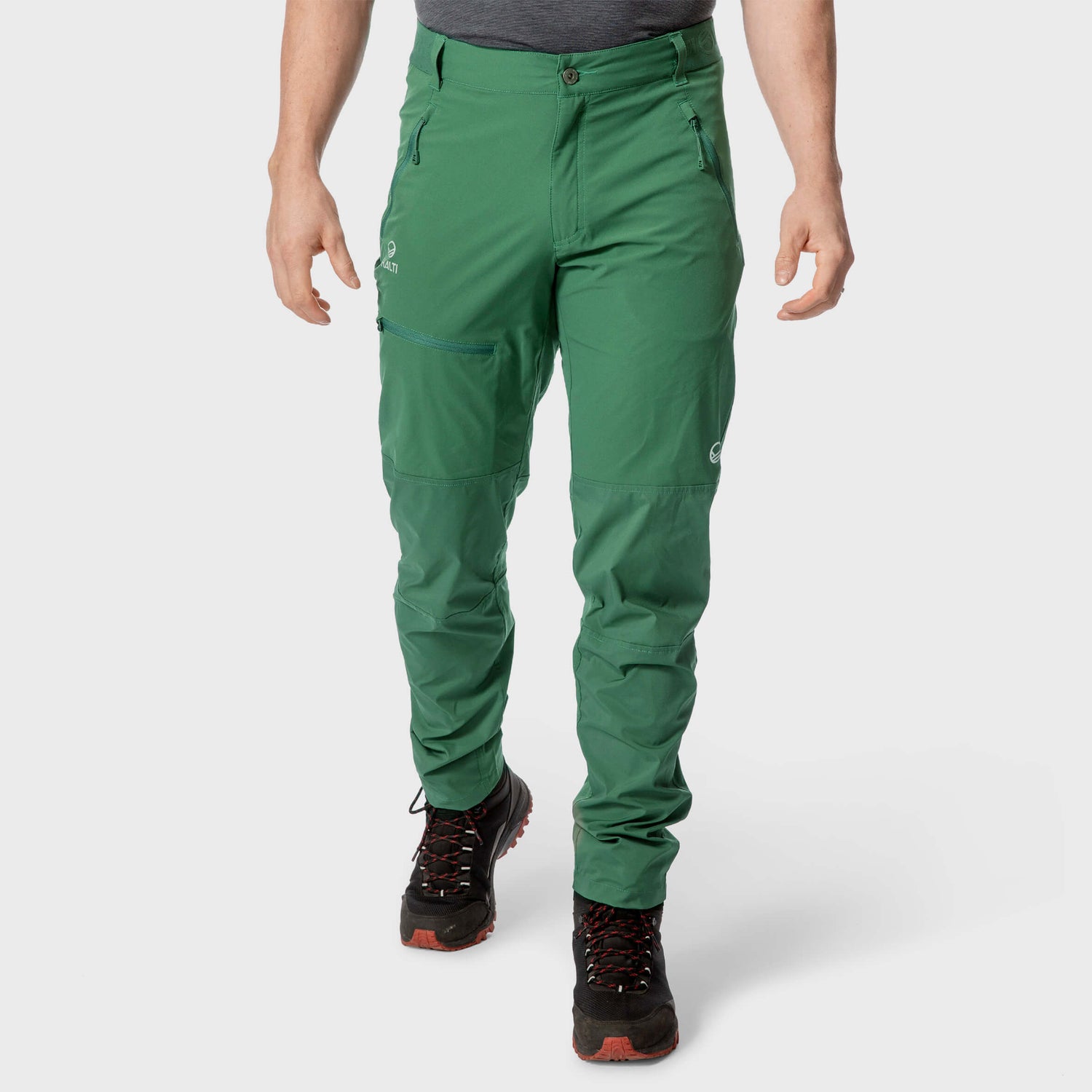 Henkilö, jolla on yllään vihreät vetoketjulliset vaellushousut ja mustat vaelluskengät, kuvattuna olkapäistä alaspäin valkoista taustaa vasten.