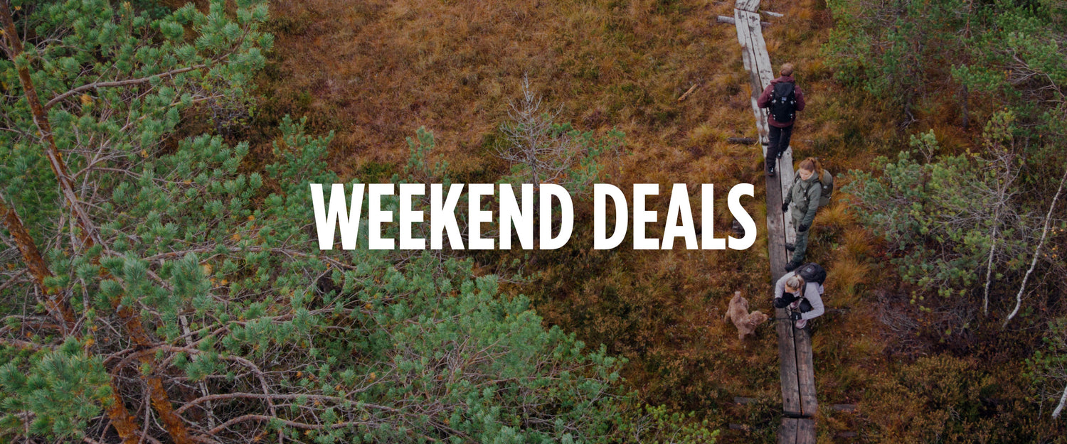 Ilmakuva kolmesta ihmisestä ja koirasta, jotka kävelevät metsässä puupolkua pitkin, WEEKEND DEALS -teksti päällä.