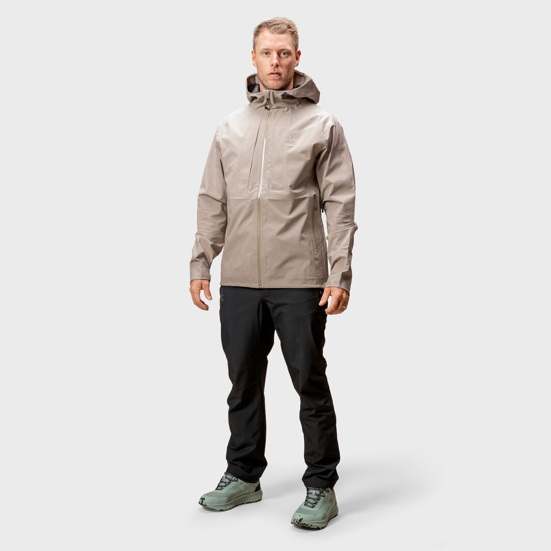 Miehellä on päällään Halti Kaarna Miesten DX 3L Kuoritakki taupe-väreissä, mustissa housuissa ja vaaleanvihreissä tennareissa.