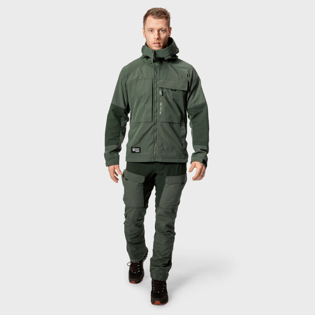 Mies Halti Hiker Miesten Ventilated Retkeilyhousuissa, vihreässä takissa ja mustissa saappaissa seisoo kasvot eteenpäin.