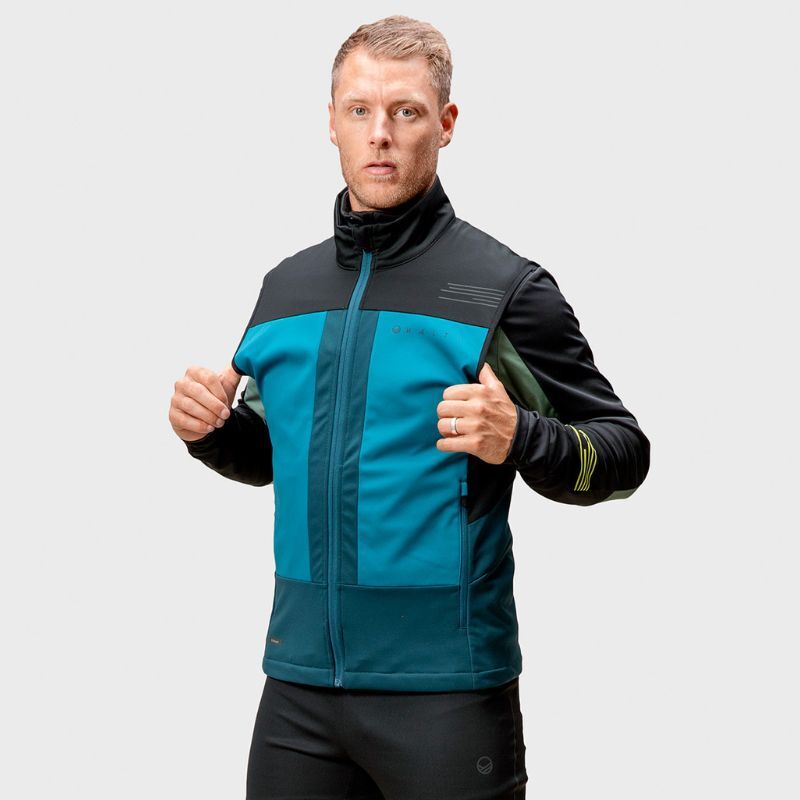 Mies poseeraa Halti Vinha Unisex -hiihtoliivissä pitäen sitä auki yksiväristä vaaleanharmaata taustaa vasten.