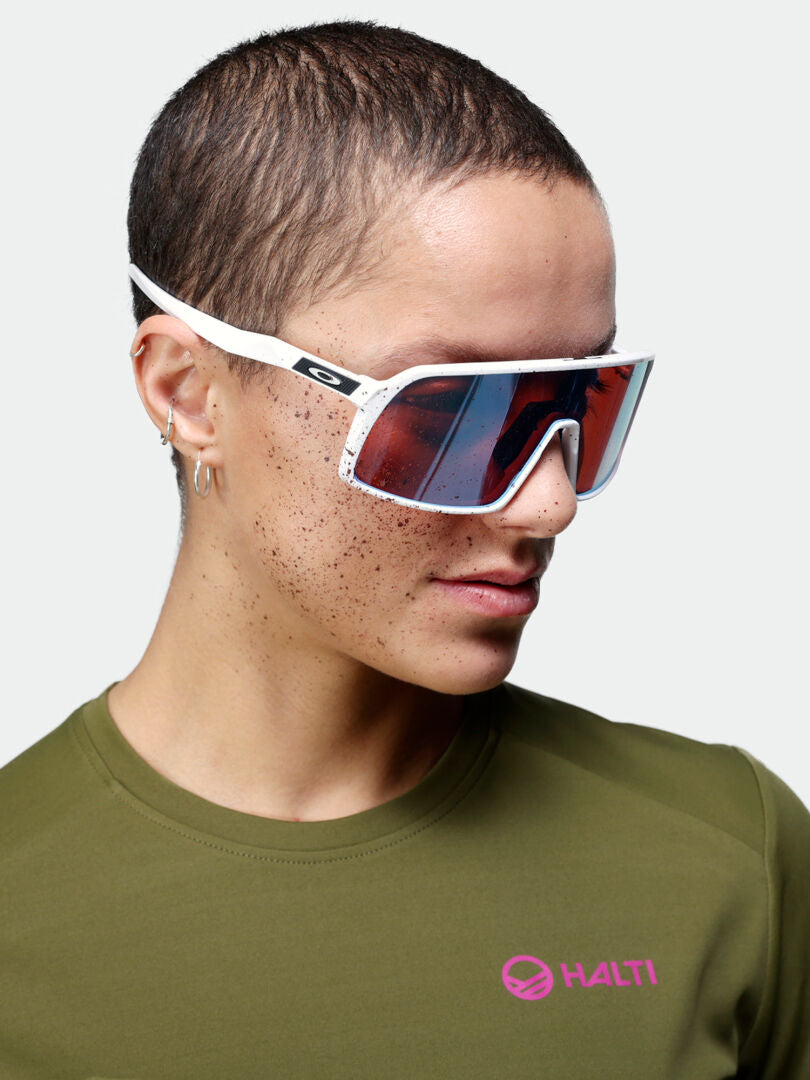 Neljä vihreää, tummansinistä, beigeä ja keltaista pitkähihaista paitaa roikkuu pyykkinarussa, joka on ripustettu kahden puun väliin metsäisellä ulkoilualueella. Auringonvalo suodattuu lehtien läpi.