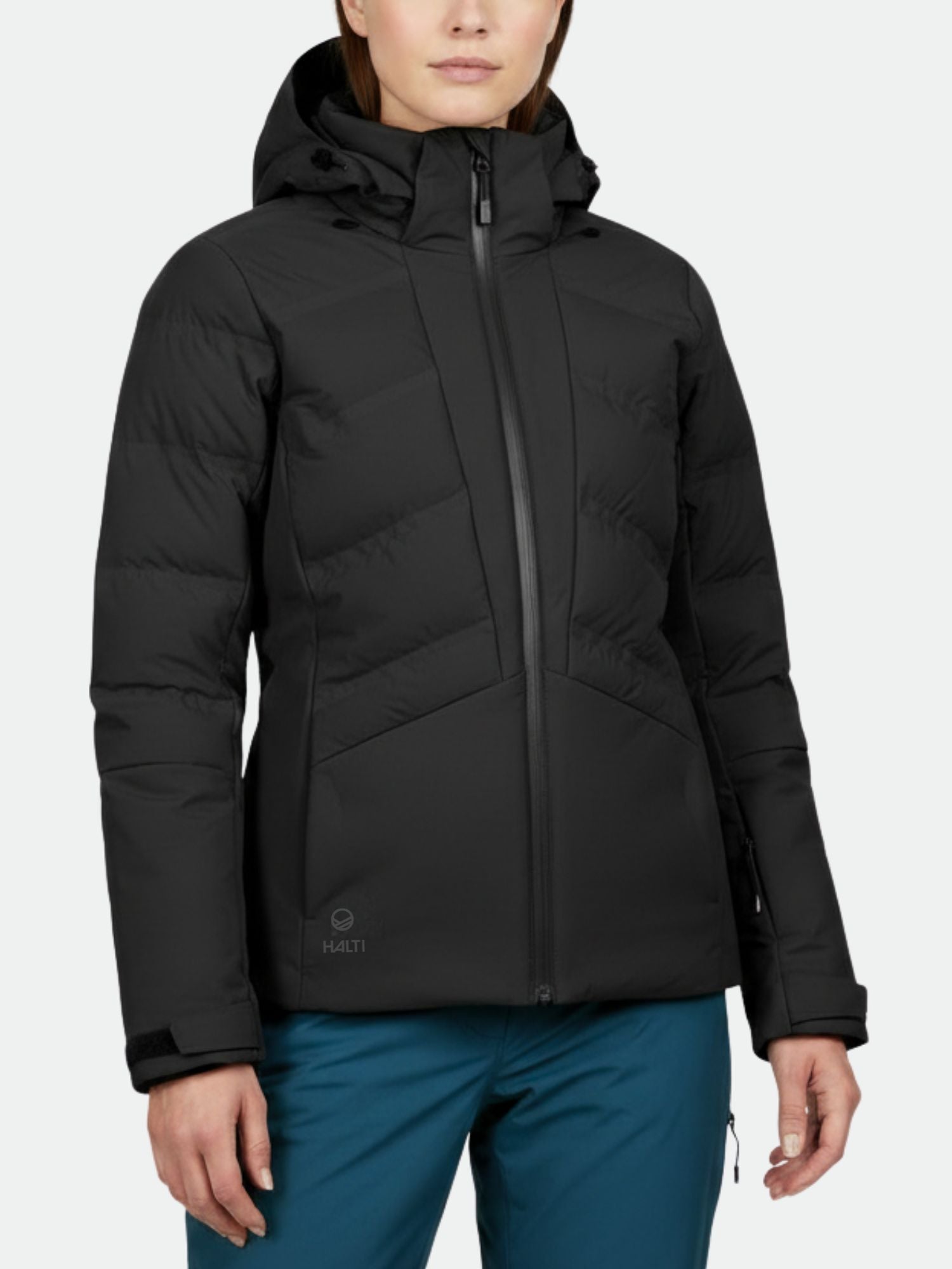 Halti Nordic Arcty Laskettelutakki Naisten ja tiilenpunaiset housut yllään oleva henkilö seisoo vaaleaa taustaa vasten.