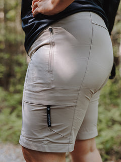 Henkilö pukeutuu metsäpolulla Halti Reissu Plus Naisten Stretch Shortsit vaalean beigen sävyyn.
