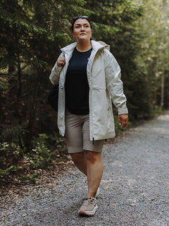 Halti Reissu Plus Naisten stretch-shortseihin, kevyeen takkiin ja mustaan paitaan pukeutunut henkilö kävelee sorapolulla.