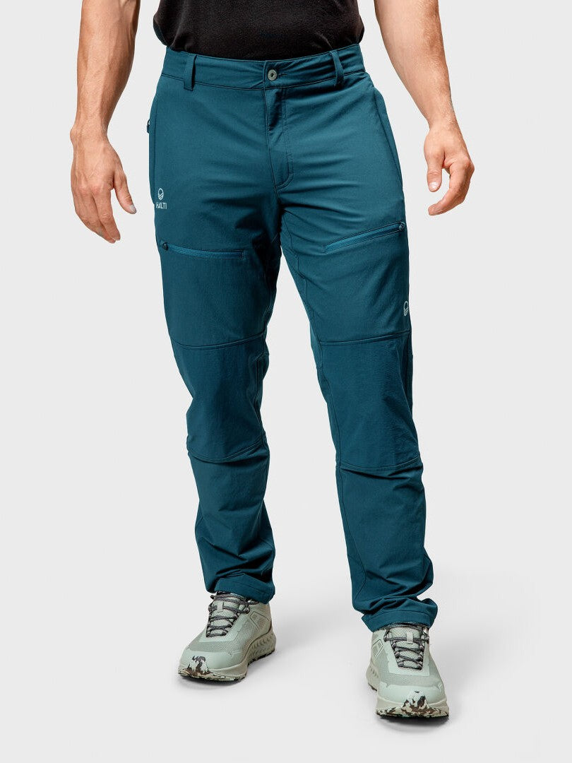 Henkilöllä on yllään tiilenpunainen Halti Pallas III Warm X-stretch ulkoiluhousut miesten yksiväristä taustaa vasten.