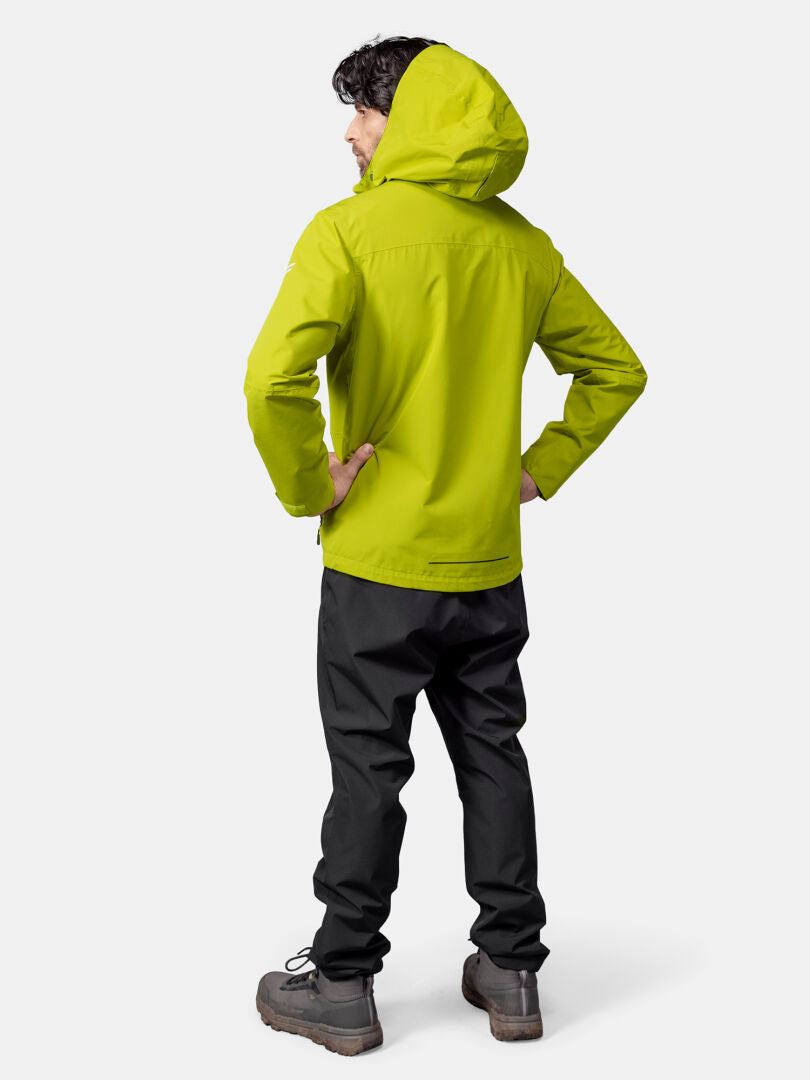 Henkilö seisoo kädet lanteilla kirkkaankeltaisessa Halti Forter DX Kuoritakki miesten, mustat housut, harmaat saappaat, kasvot poispäin.