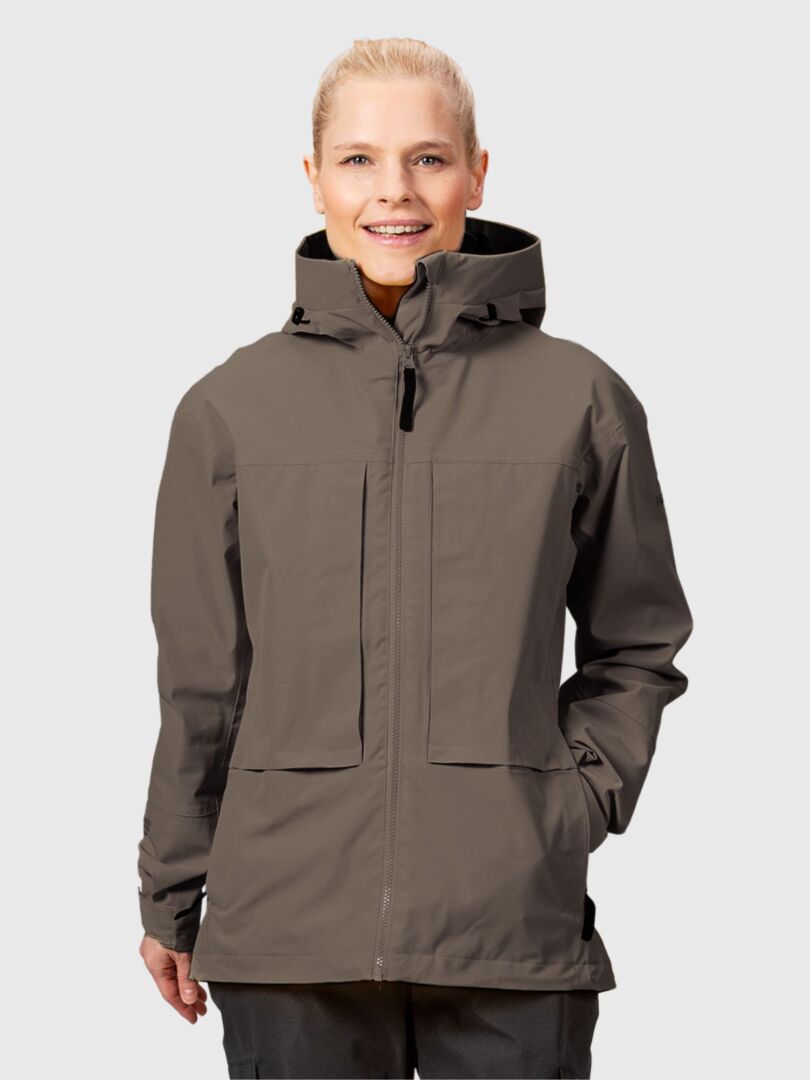 Naisella on yllään taupe-värinen, hupullinen Halti Hiker II DrymaxX Kuoritakki Naisten -takki, jossa on edessä vetoketju ja suuret taskut.