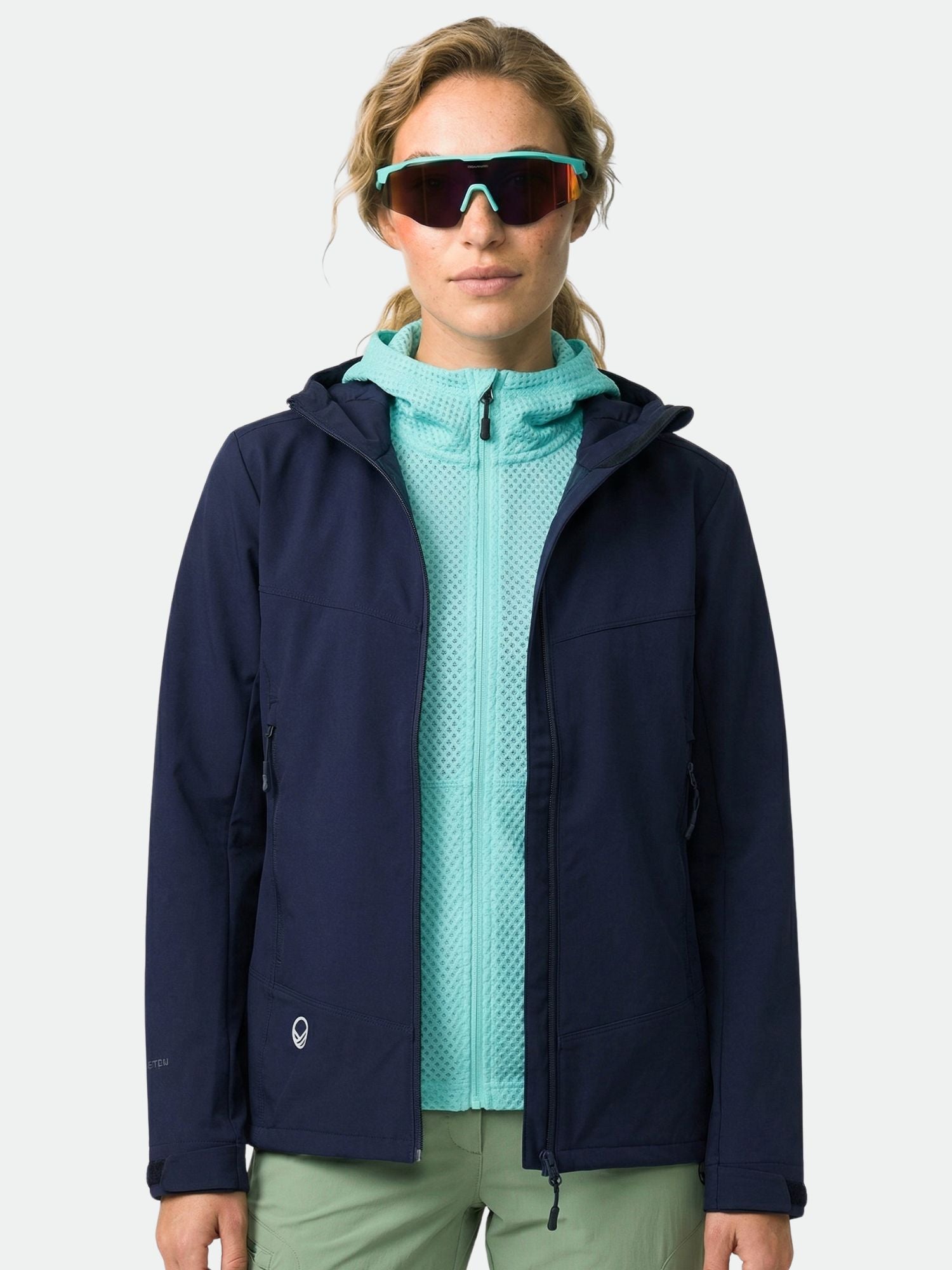 Henkilöllä on päällään tummansininen Halti Pallas Evo Brushed X-stretch Takki Naisten, vihreät housut ja aurinkolasit kameraan päin.