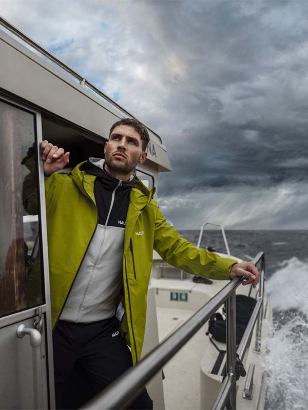 Halti Staala DX Kuoritakki Miesten mies seisoo veneessä ja katselee myrskyistä merta pilvisen taivaan alla.