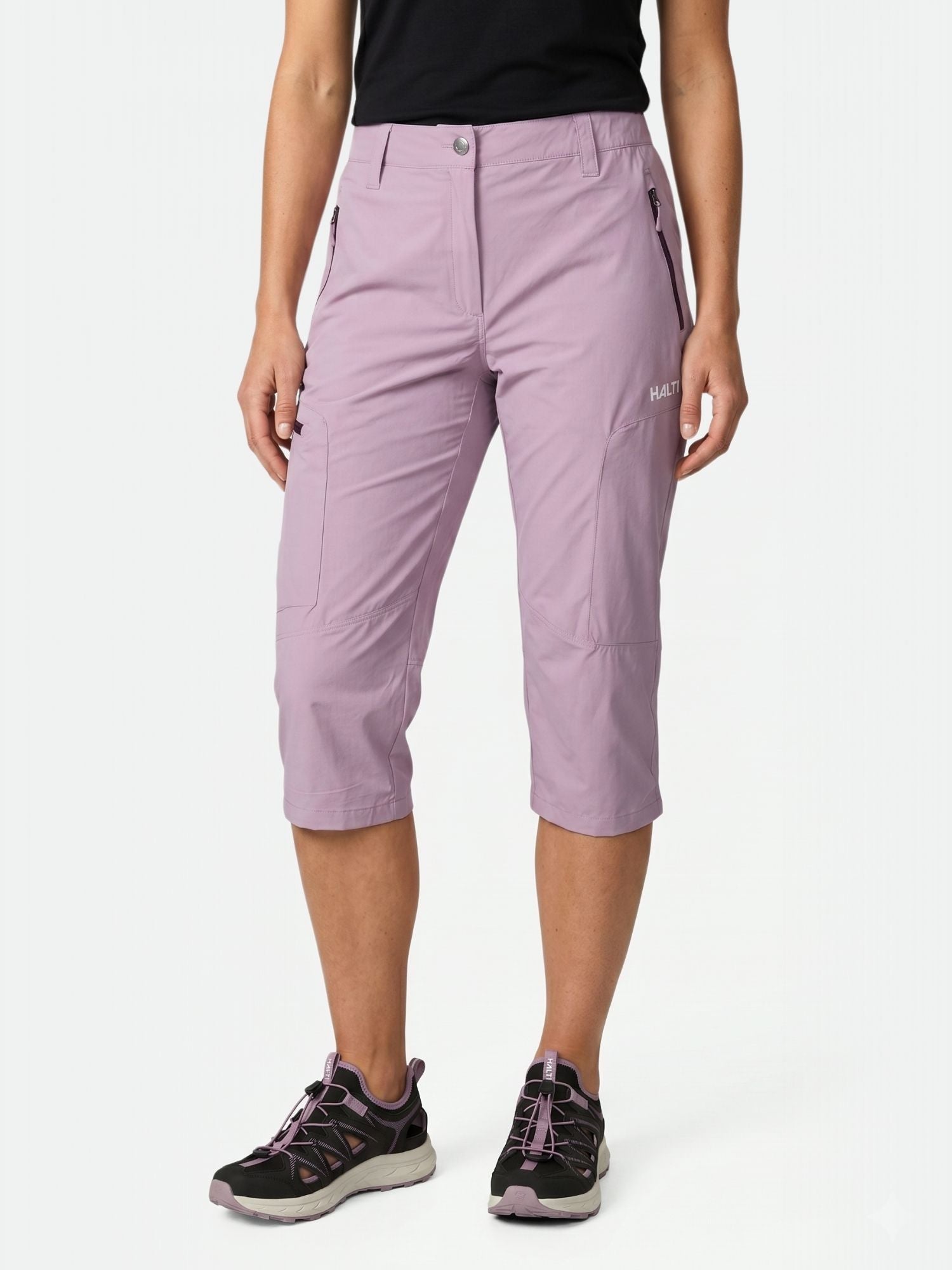 Henkilöllä on yllään vaaleanvioletti Halti Pallas Cool X-stretch Caprit Naisten (UPF 90+), musta T-paita ja mustat vaelluskengät.