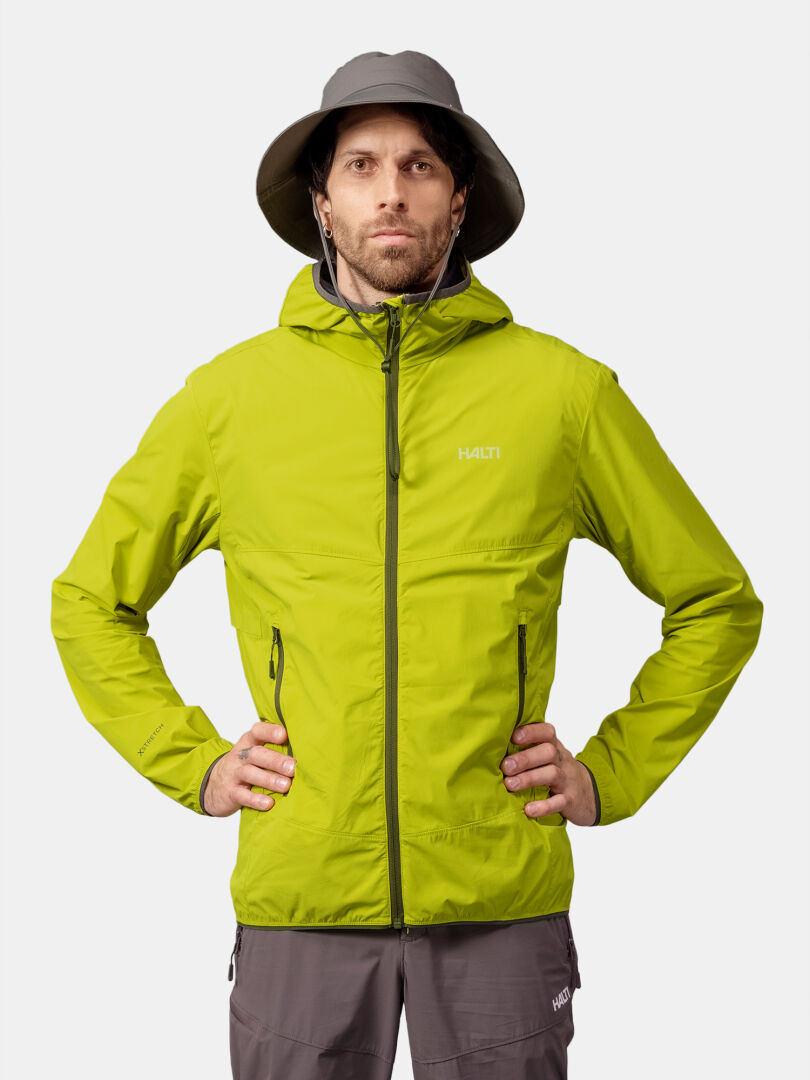 Mies vihreässä Halti Pallas Cool X-stretch Takki Miesten ja harmaissa housuissa seisoo kädet lanteilla, valmiina päiväretkille.