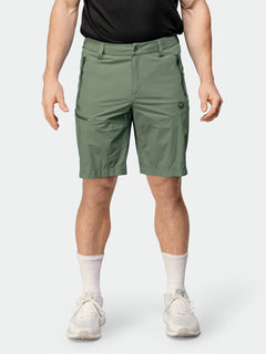 Henkilöllä on yllään Halti Pallas Cool X-stretch Shortsit Miesten vihreä, musta paita ja valkoiset lenkkarit.