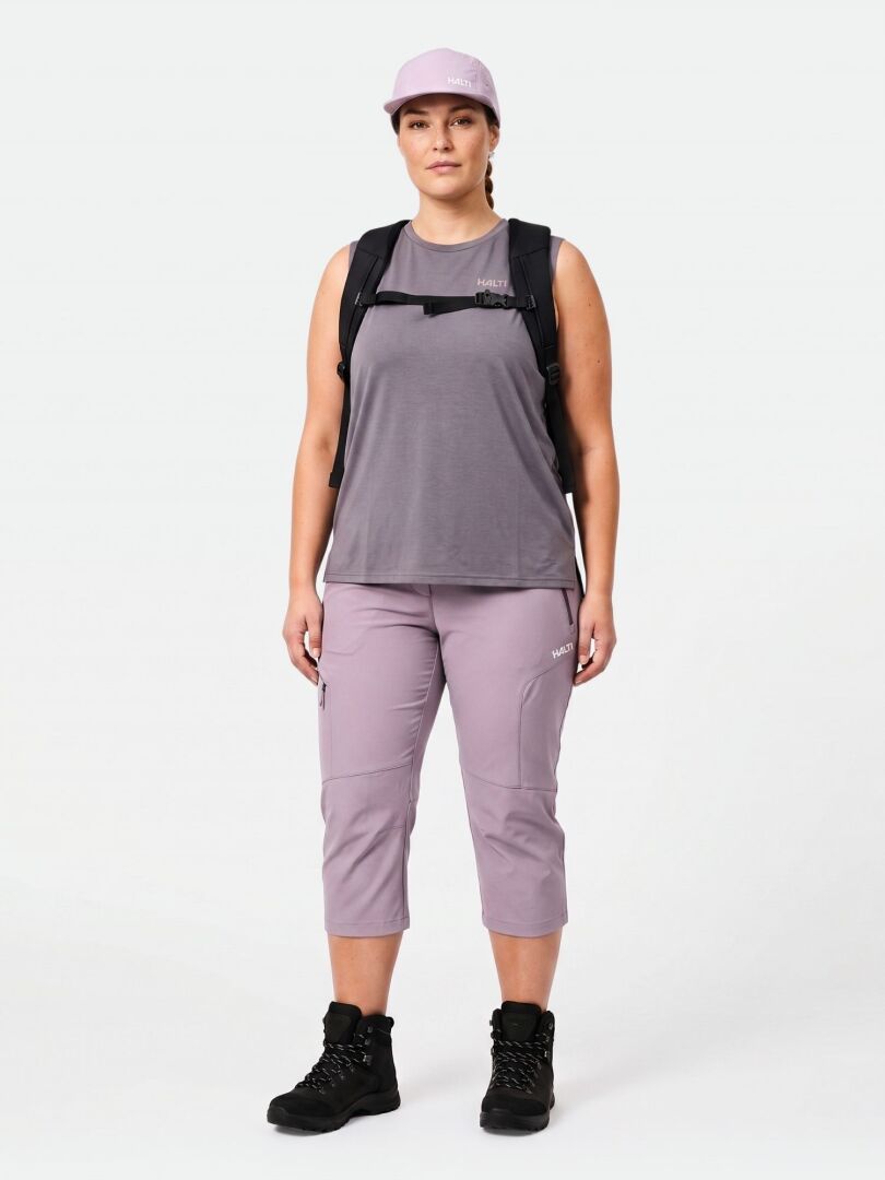 Edessä seisoo henkilö, jolla on laventelilakki, hihaton toppi, Halti Pallas Cool X-stretch Caprit, musta reppu ja vaelluskengät.