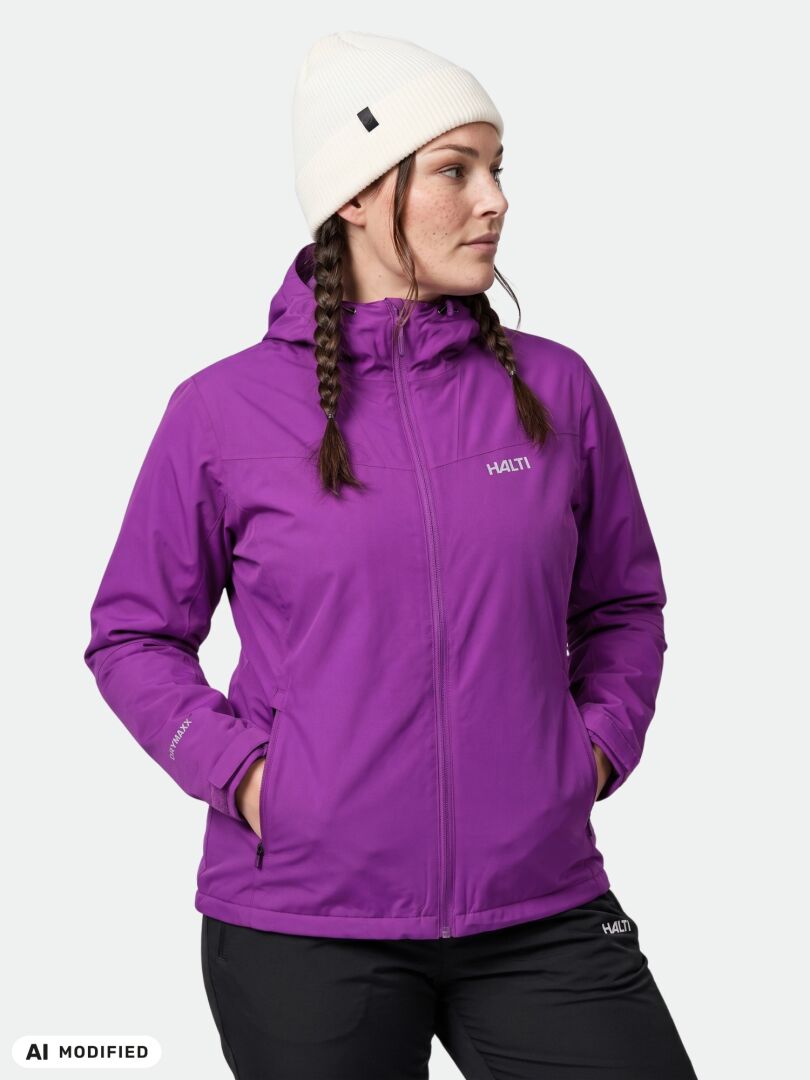 Henkilöllä on yllään Halti Finholma X-stretch Takki Naisten Plus -takki ja valkoinen pipo, kädet taskussa, ja hän on kääntynyt hieman sivulle.