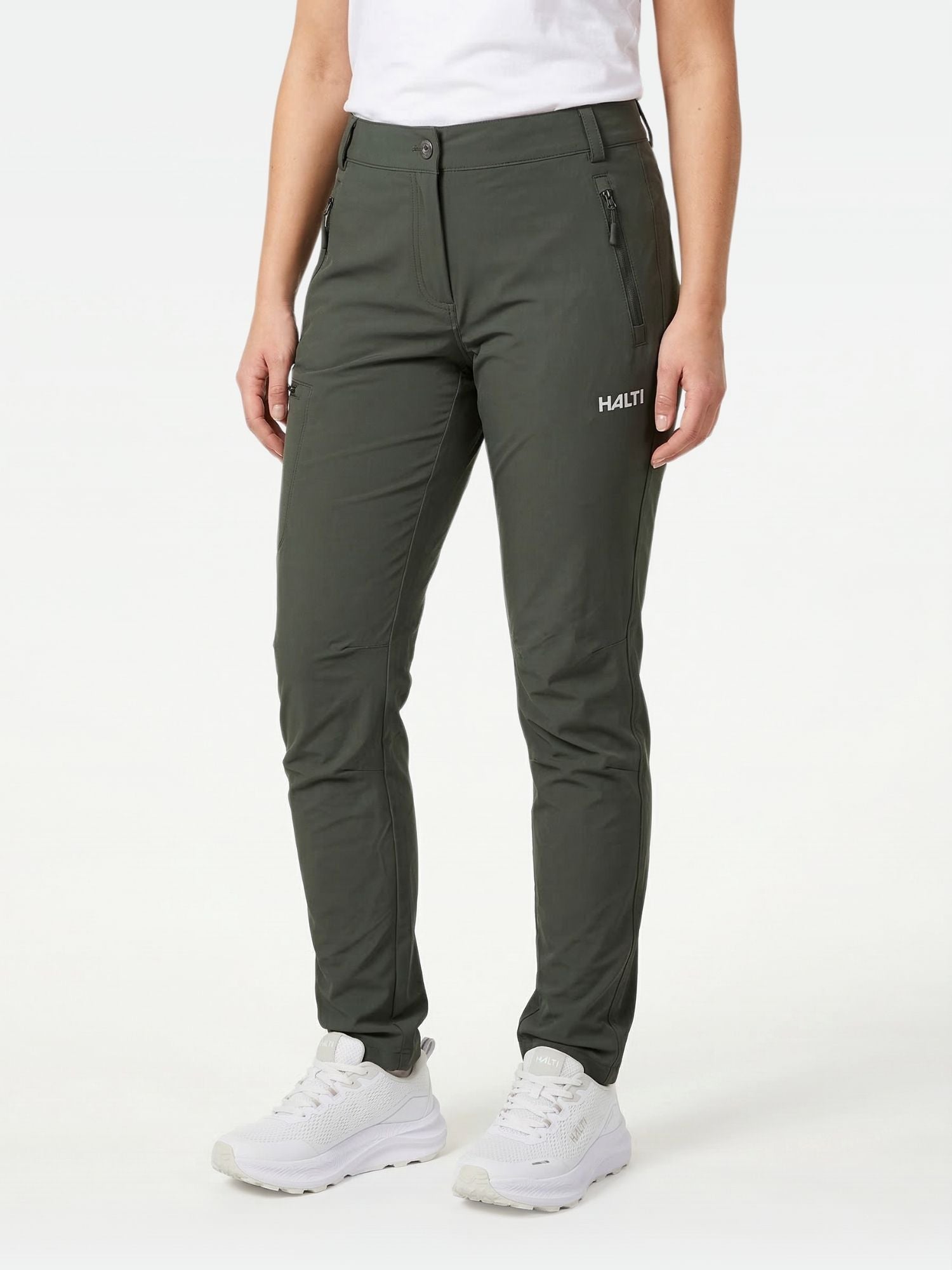 Henkilöllä on yllään tummanvihreät Halti Pallas X-stretch Ulkoiluhousut Naisten, valkoiset lenkkarit ja valkoinen t-paita.