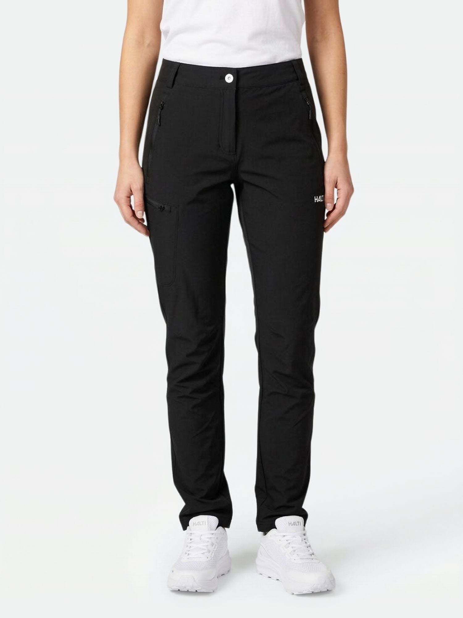 Henkilö, jolla on Halti Pallas X-stretch Ulkoiluhousut, valkoiset lenkkarit ja valkoinen paita, seisoo vaaleaa taustaa vasten.