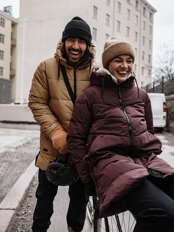 Halti Linjat Parkatakki Naisten nainen hymyilee pyörällä ulkona miehen vieressä; molemmilla on talvitakit ja pipot.