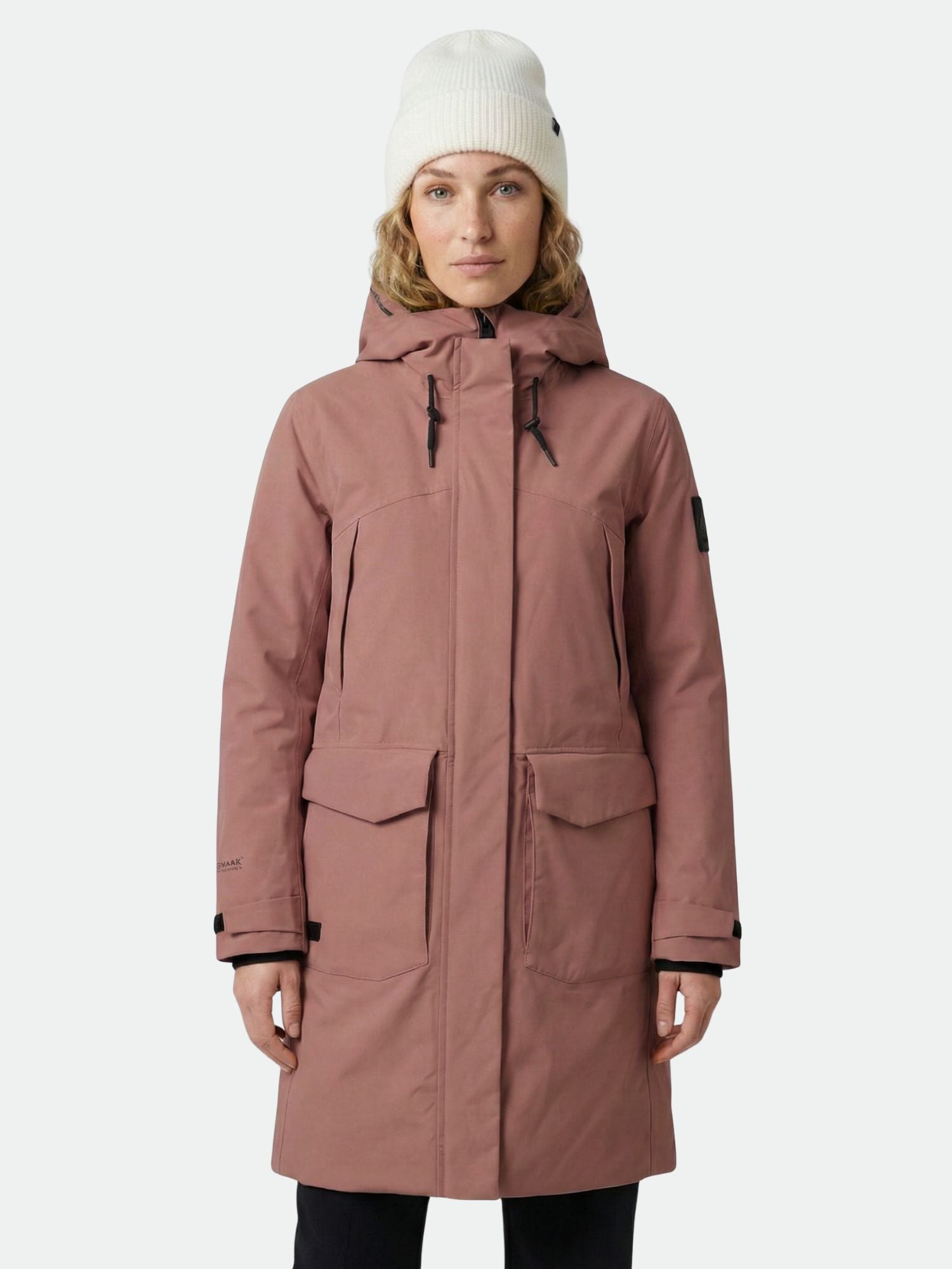 Henkilöllä on päällään violetti Halti Bergga DX Talvitakki Naisten ja valkoinen pipo, kasvot eteenpäin tavallista taustaa vasten.