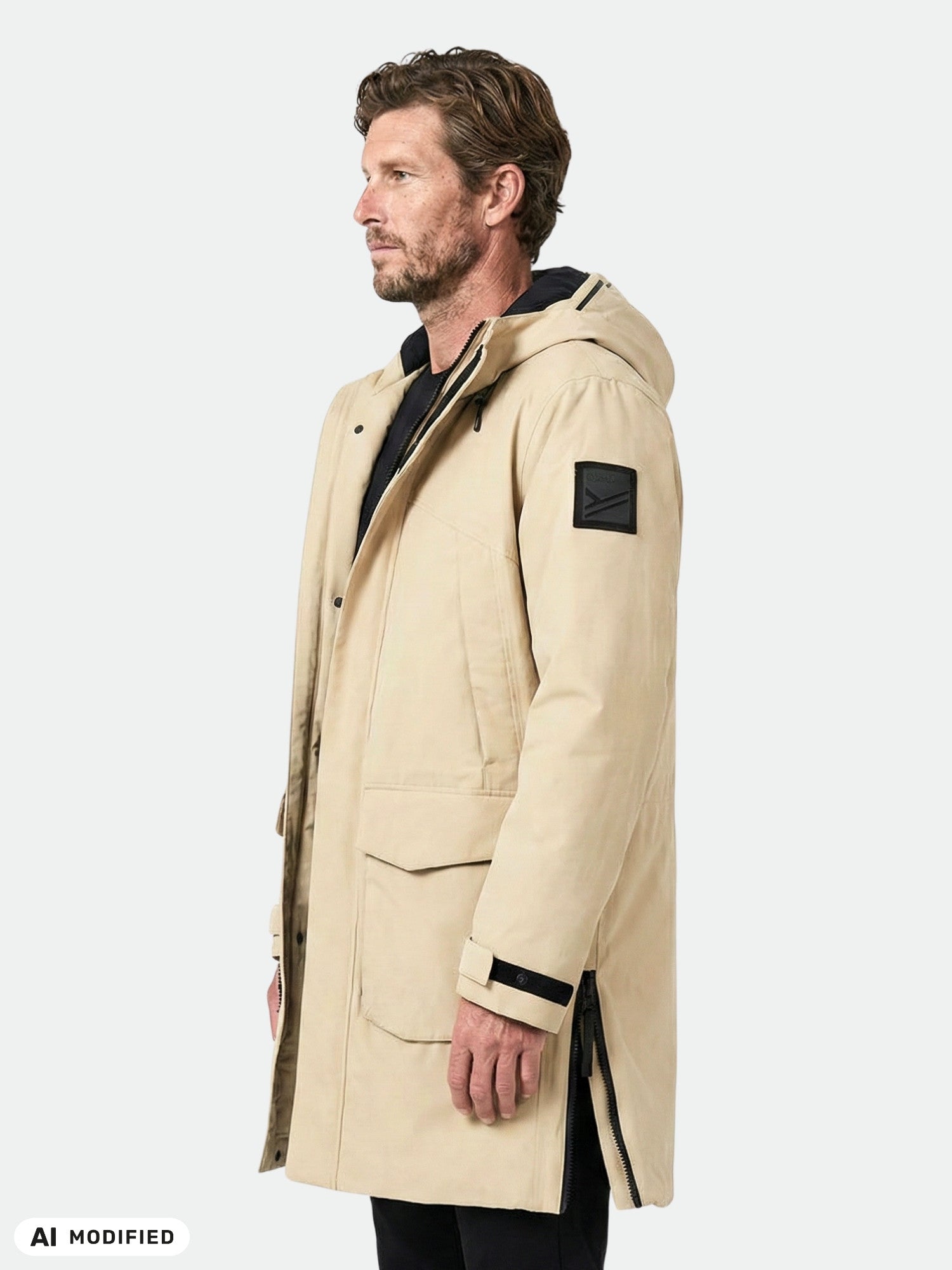 Mies, jolla on yllään Halti Bergga DX -talvitakki (miesten malli), beige, mustalla laastarilla, seisoo profiilissa yksiväristä taustaa vasten.