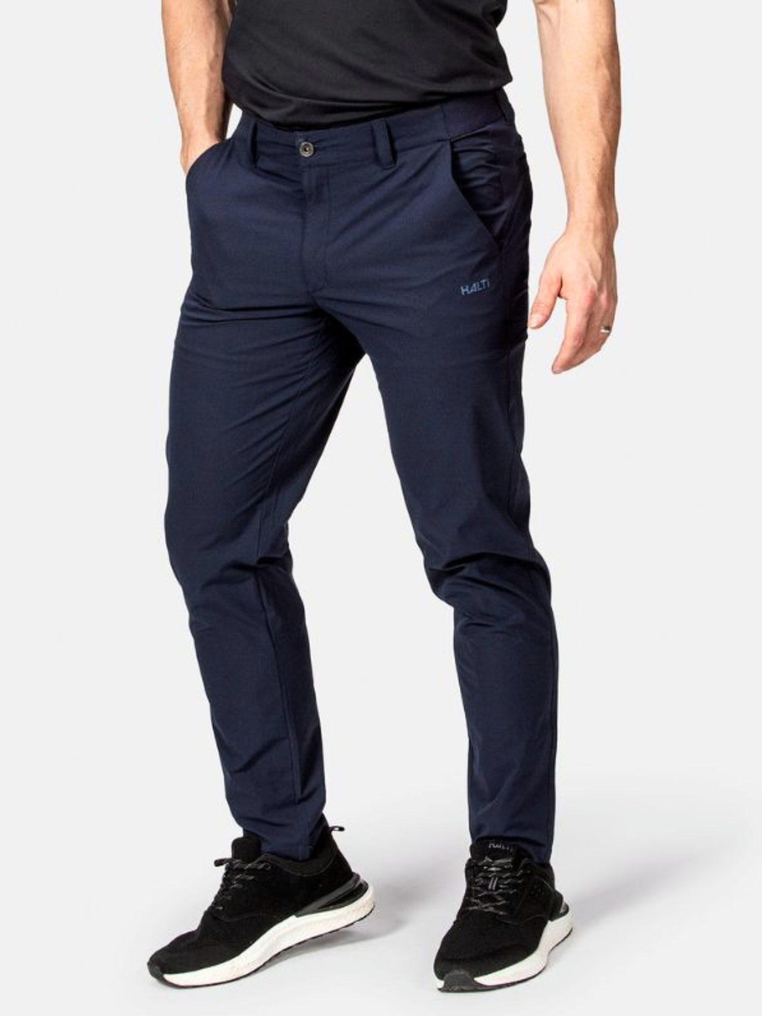 Mies, jolla on Halti Drive X-stretch Chinot ja musta t-paita, kädet taskuissa, seisoo mustilla lenkkareilla.