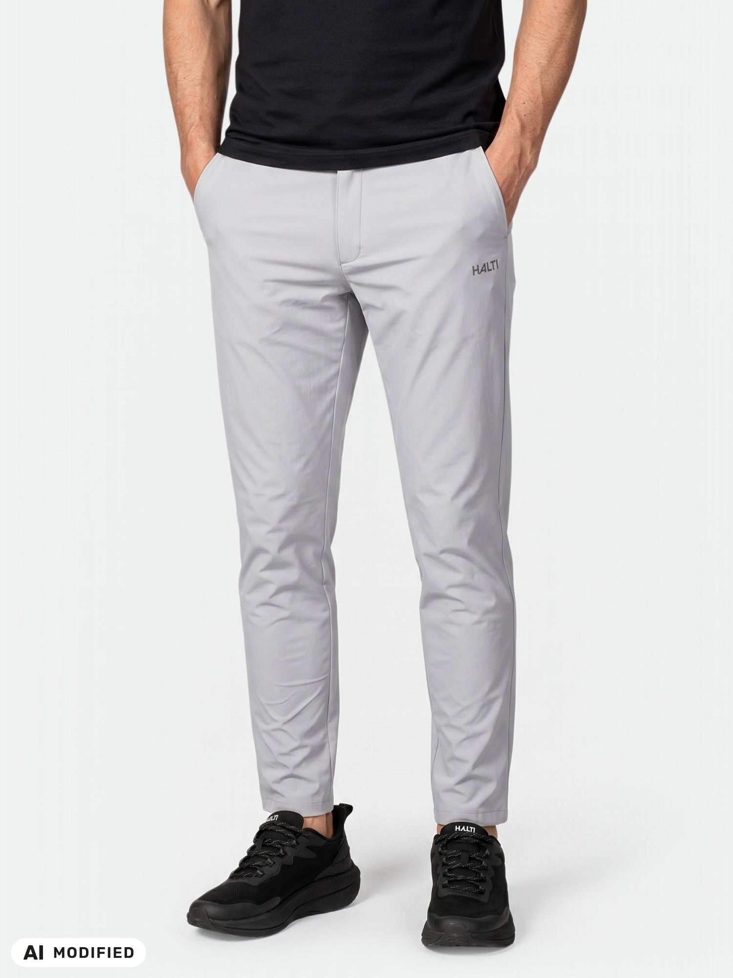 Yllään vaaleanharmaat Halti Drive X-stretch -chino-housut, mustat kengät ja musta paita, kädet taskussa.